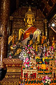 Wat Xieng Thong temple in Luang Prabang, Laos.  The main Buddha of the sim sits on a platform, surrounded by smaller statues, candles, and offerings. 